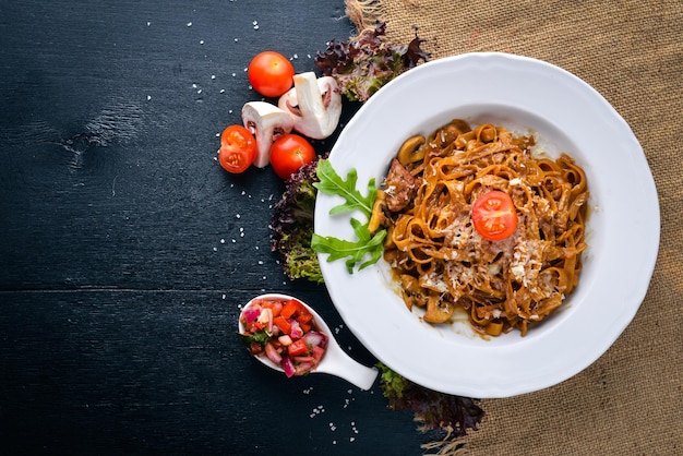 Foto pasta con tomates cherry, aceitunas y champiñones con queso parmesano. comida italiana. sobre una superficie de madera negra. espacio libre para su texto. vista superior.