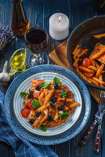 Pasta con tomates cherry, mozzarella y aceitunas espinacas, vino y aceite en una mesa de madera. Estilo rústico.