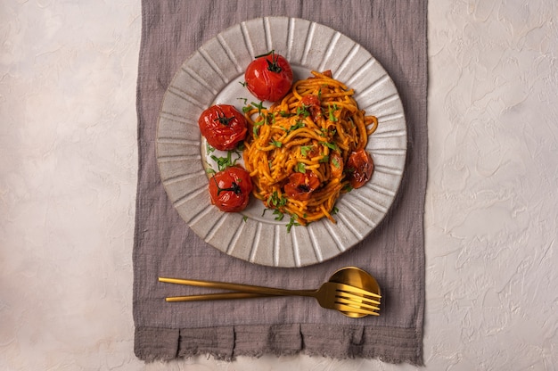 Pasta con tomates cherry, queso y romero servido en plato con cuchara y tenedor y servilleta