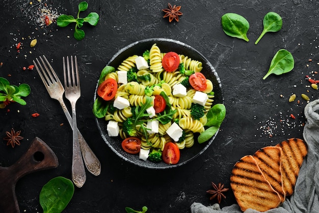 Pasta con tomates espinacas y queso feta En un plato negro sobre un fondo de madera Vista superior Espacio libre para su texto Plano