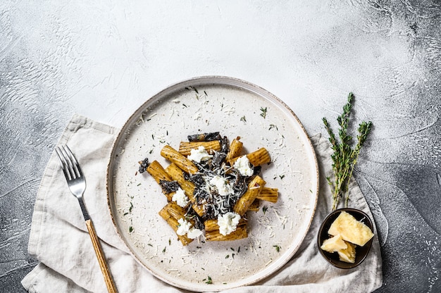 Pasta Tortiglioni mit schwarzem Trüffel, weißem Pilz, Sahnesauce und Ricotta. Grauer Hintergrund, Draufsicht. Platz für Text