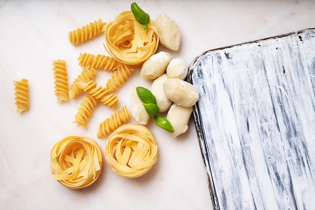 Pasta tradicional italiana: Tagliatelle, fusilli y ñoquis decorados con hojas de albahaca. Concepto de comida italiana. Vista superior. Lay Flat