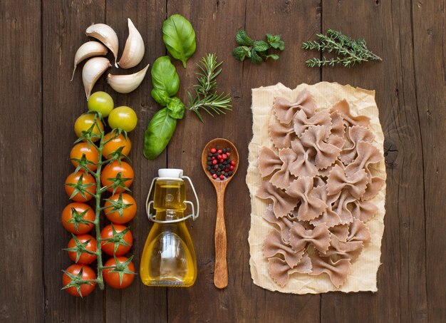 Pasta de trigo integral, verduras, hierbas y aceite de oliva en la vista superior de madera