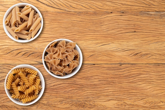 Pasta variada de trigo integral en tazones sobre una mesa de madera con espacio para copiar