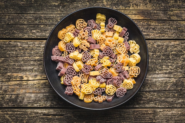 Pasta de varias formas aterradoras Pasta de Halloween sin cocinar en un plato sobre una mesa de madera Vista superior