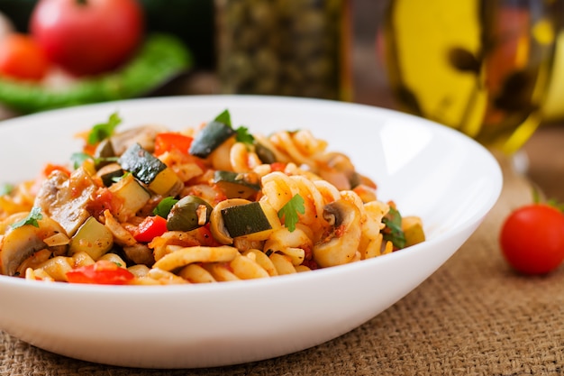 Pasta de verduras vegetariana Fusilli con calabacín, champiñones y alcaparras en un tazón blanco sobre mesa de madera