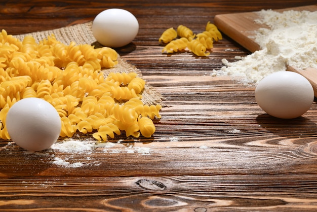 Pastas crudas e ingredientes para pasta sobre fondo de madera.