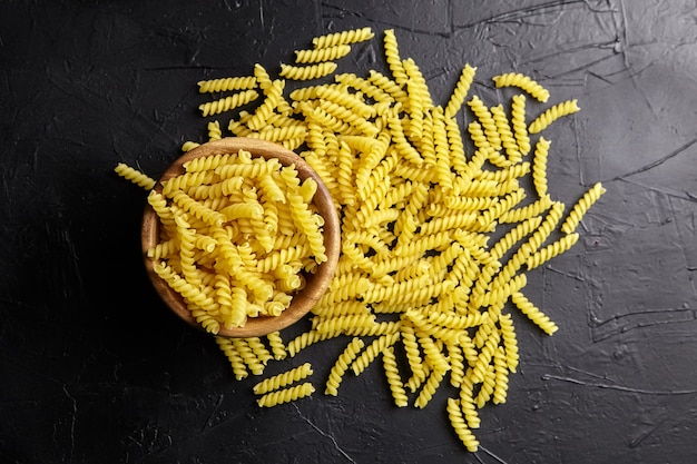 Pastas Girandole en cuenco de madera en la vista superior de la mesa de piedra negra