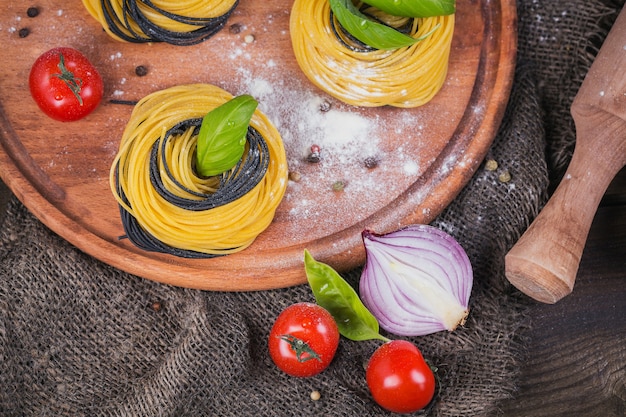 Pastas italianas crudas con ingredientes. Tomates cherry, espaguetis crudos, cebolla roja y hierbas sobre una mesa de madera rústica oscura. Concepto de cocina. Vista superior