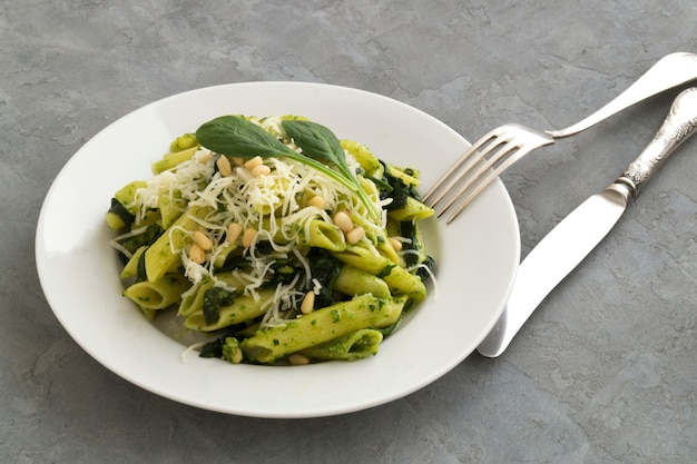 Pastas de Penne con espinaca en fondo gris.