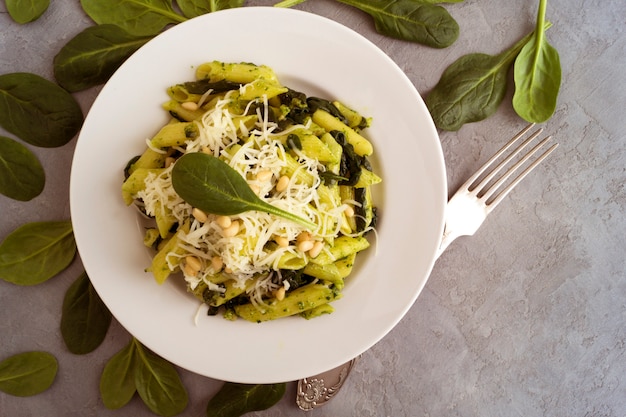 Foto pastas de penne con espinaca en fondo gris.