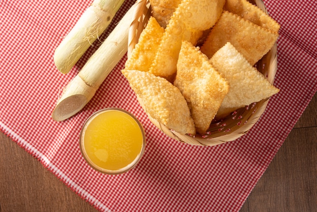 Pastéis fritos brasileiros, um copo de caldo de cana e canas posicionadas sobre uma toalha de mesa quadriculada