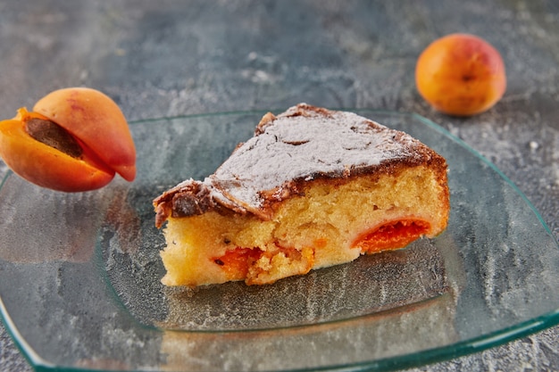 Pastel de albaricoque y almendra con pieza cortada sobre placa de vidrio sobre fondo de hormigón.