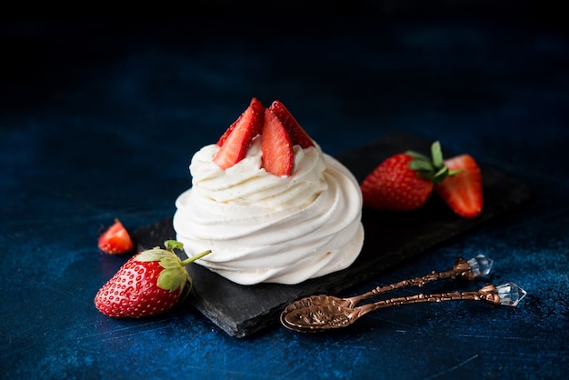 Pastel de Anna Pavlova con crema y fresas frescas sobre un fondo oscuro