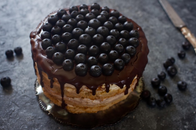 Pastel de arándanos vegano decorado con glaseado de chocolate y bayas en una mesa de piedra oscura