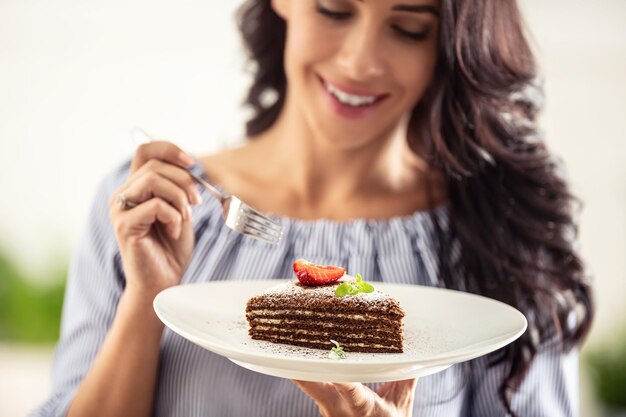 Foto pastel blanco adn marrón en capas con fresa y hoja de menta en la parte superior sostenido por una mujer con un tenedor