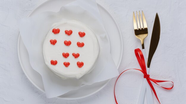 Pastel blanco con corazones en un plato blanco con cuchillo y tenedor