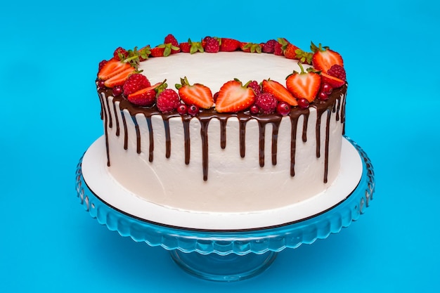 Pastel blanco de cuajada decorado con bayas y frambuesas y rociado con chocolate sobre un fondo azul dulces pasteles caseros