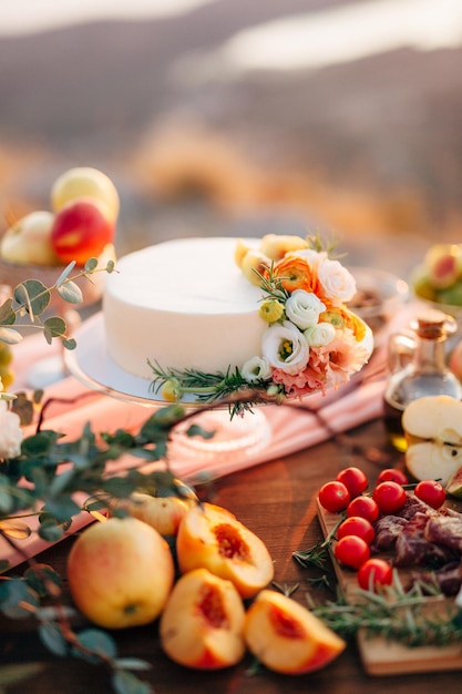 Pastel de boda decorado con flores se encuentra sobre una mesa entre frutas y verduras