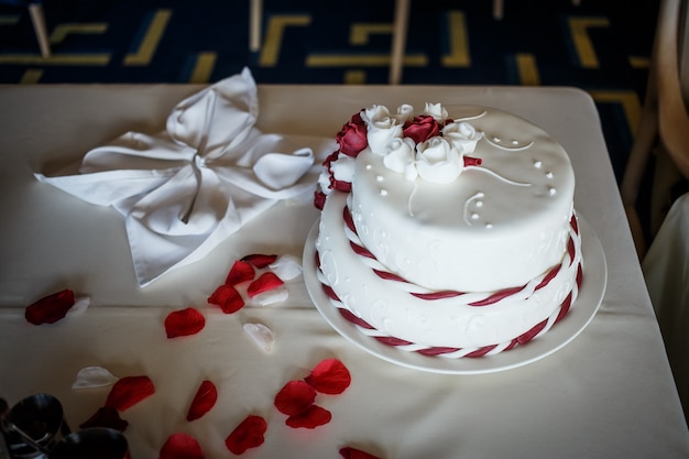 Pastel de boda sobre la mesa con rojo pertals de rosa roja. Ceremonia de matrimonio