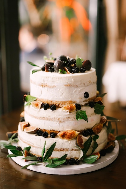 Pastel de boda de tres niveles decorado con moras, higos, ciruelas y hojas verdes se encuentra sobre la mesa