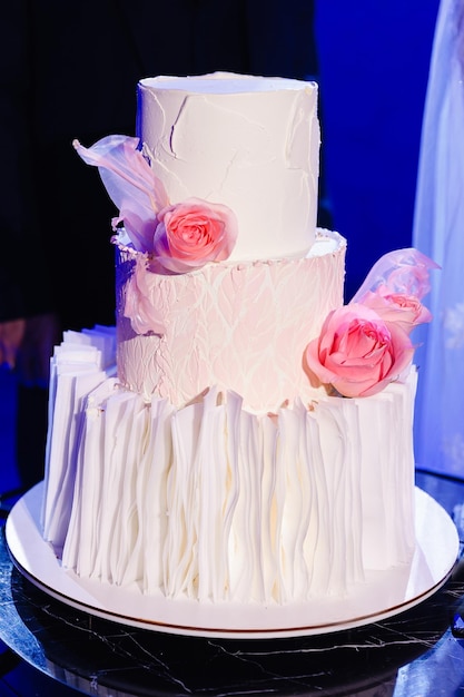 Un pastel de bodas adornado con rosas blancas contra un fondo azul añade elegancia a la atmósfera de