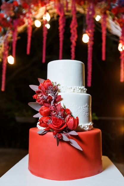 Pastel de bodas blanco decorado con flores frescas de pie en el fondo del arco de la boda