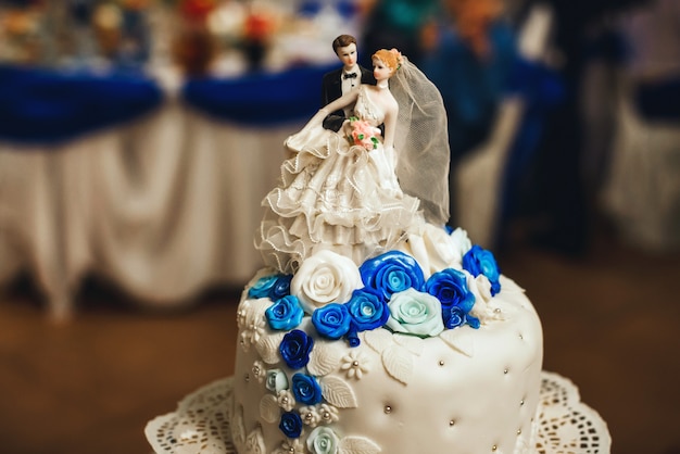 Pastel de bodas blanco decorado con rosas azules con niveles y una figura de la novia y el novio
