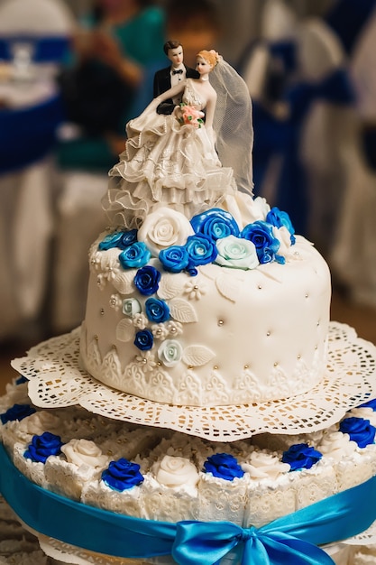 Pastel de bodas blanco decorado con rosas con tres niveles una figura de la novia y el novio