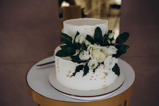 Pastel de bodas blanco de tres niveles decorado con flores de masilla sobre una mesa de madera blanca Imagen para un menú o un catálogo de confitería con espacio para copiar