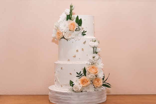 un pastel de bodas blanco de varios niveles sobre una base de plata y flores rosadas en la parte superior