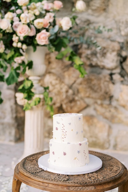 El pastel de bodas se encuentra en una mesa de madera cerca de un ramo de flores en un jarrón en un pedestal