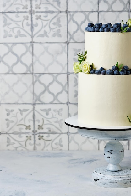 Un pastel de bodas grande y elegante. Un pastel de dos niveles para unas hermosas vacaciones. Pastel blanco decorado con arándanos frescos y rosas blancas.