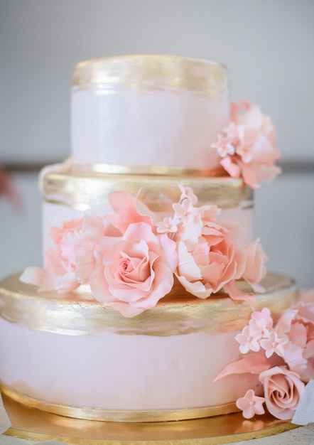 Pastel de bodas de lujo cubierto con esmalte dorado y decorado con rosas rosadas