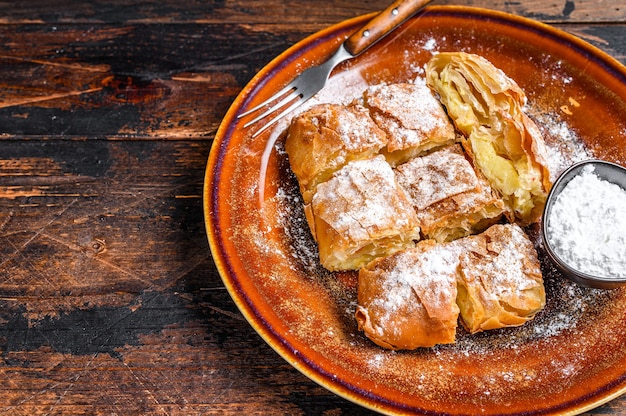 Pastel de Bougatsa griego en rodajas con masa filo y crema pastelera de sémola. Oscuro