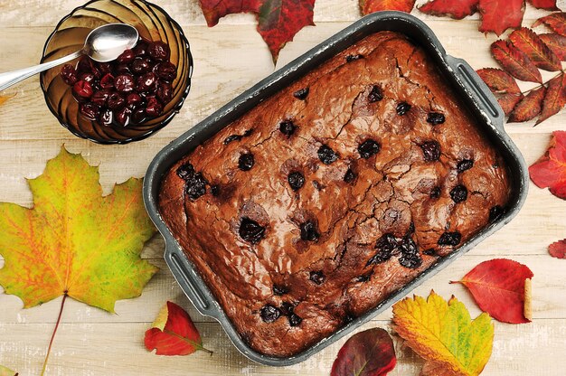 Pastel de brownie con cerezas sobre un fondo de madera con hojas de otoño - vista superior