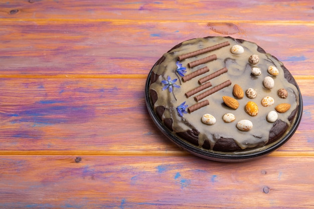 Pastel de brownie de chocolate casero con crema de caramelo y almendras sobre un fondo de madera de color.