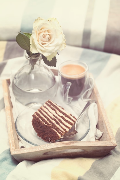 Pastel con café y flores en bandeja en la cama