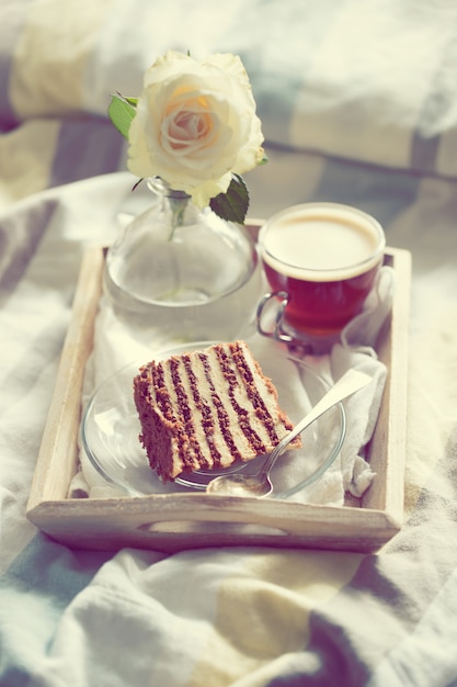 Pastel con café y flores en bandeja en la cama