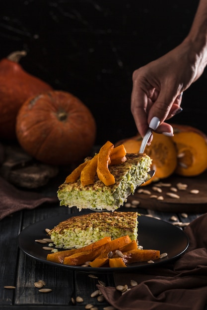 Pastel de calabacín con calabaza al horno en una espátula en manos de las mujeres en la cocina, en un primer plano de copyspace de madera oscura con copyspace.