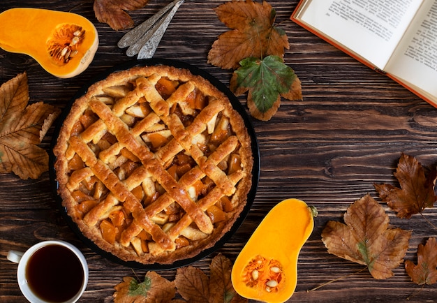 Pastel de calabaza casero. Halloween y Acción de Gracias. Dulces de calabaza de vacaciones. Fondo de otoño de madera, hojas secas, calabaza cortada, taza de té y un libro. Vista superior. Copia espacio