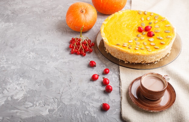 Pastel de calabaza dulce americano tradicional decorado con bayas rojas de espino y semillas de calabaza con una taza de café sobre un fondo de hormigón gris. Vista lateral, copia espacio.