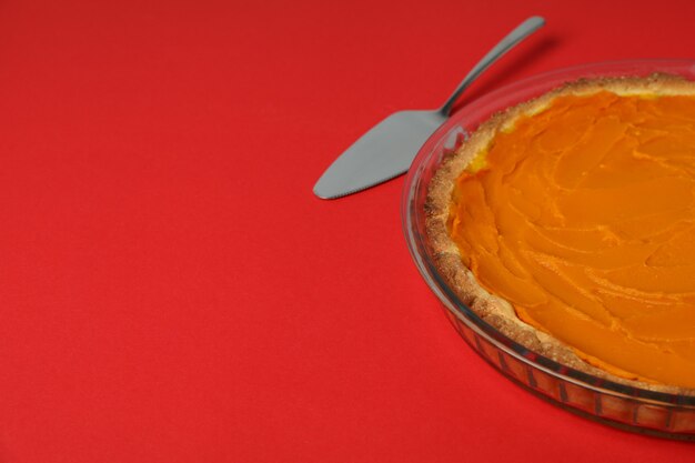 Pastel de calabaza y espátula de pastel sobre fondo rojo.