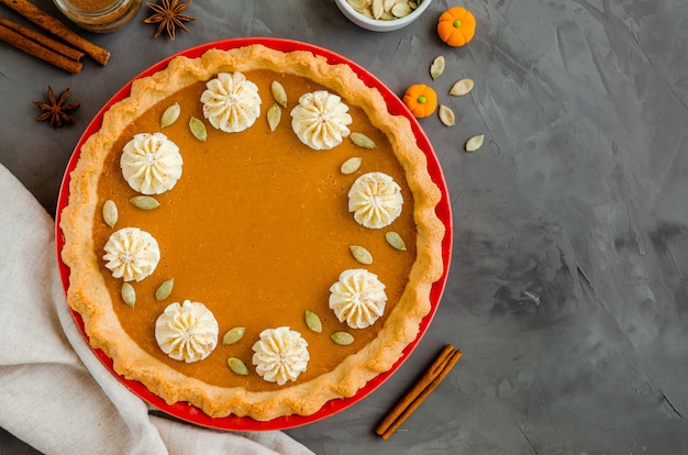 Pastel de calabaza festivo tradicional con especias, crema batida y semillas encima de una piedra oscura