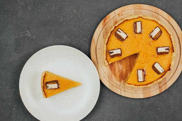 Pastel de calabaza en una tabla de madera redonda y un pedazo de pastel en un plato blanco.