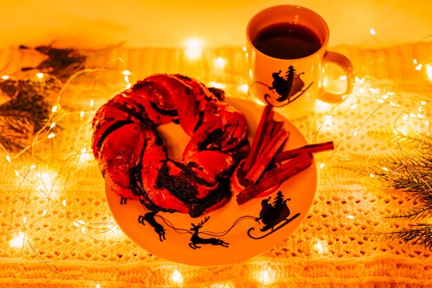Pastel y canela en un plato con santa y ciervos en el fondo de las luces de año nuevo junto a una taza