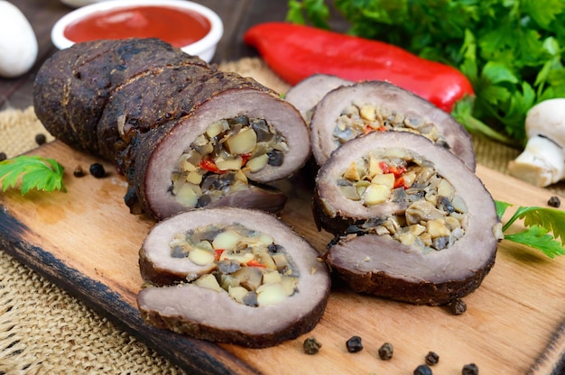 Pastel de carne (rollo) relleno de champiñones, pimiento dulce y salsa de tomate sobre un fondo de madera oscura. Plato festivo