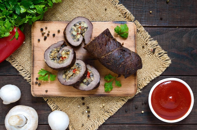 Pastel de carne (rollo) relleno de champiñones, pimiento dulce y salsa de tomate sobre un fondo de madera oscura. Vista superior. Plato festivo