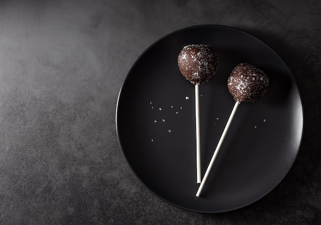 Pastel de chocolate aparece decorado con destellos en un plato oscuro. muro de hormigón oscuro