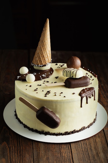 Pastel de chocolate blanco decorado con paleta en palo, cono de galleta y bolas de chocolate